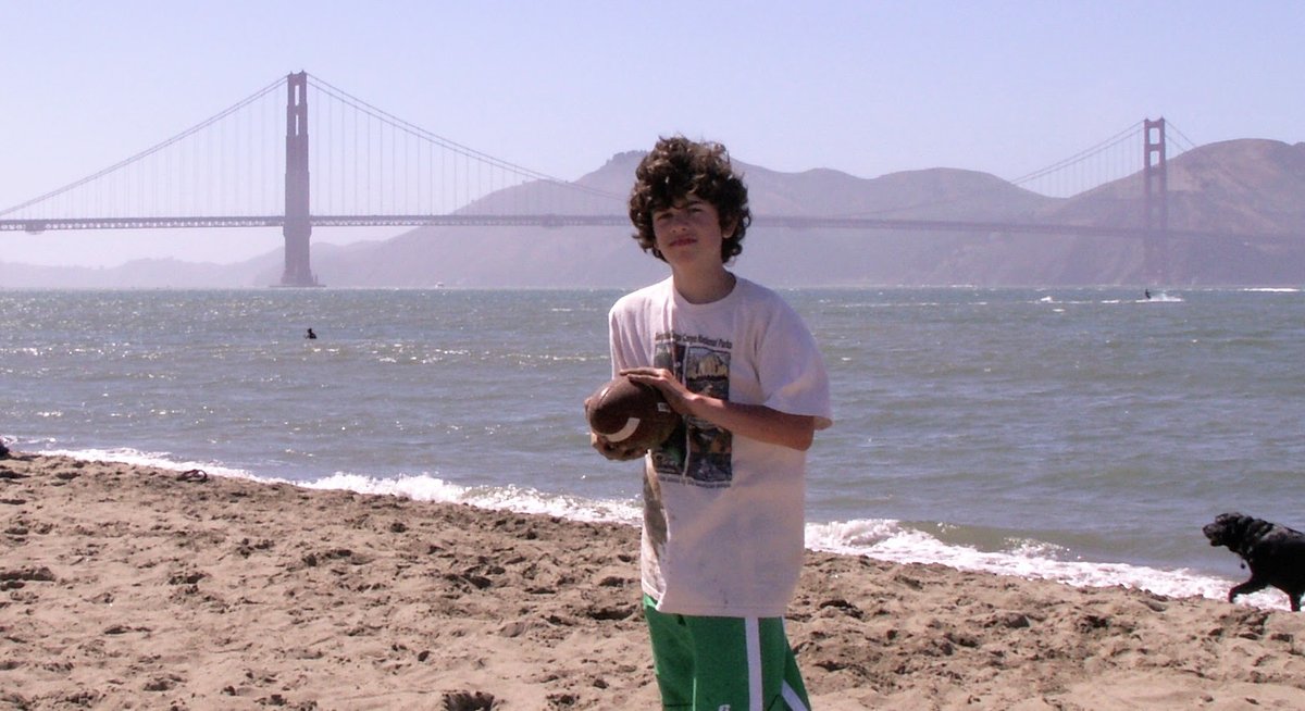 A young Jack Phillips holding a football on a beach in front of the Golden Gate Bridge, 2006